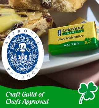 Close up of a hot cross bun, cut in half with butter on top. Next to two packs of Lakeland Dairies salted butter portions. Includes Craft Guild of Chef logo and text reads: 