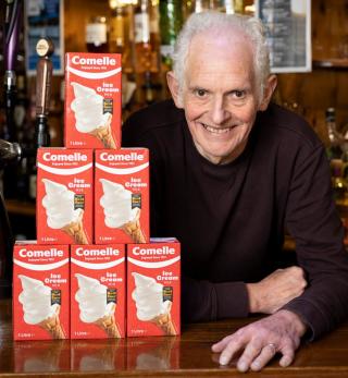 6 Packs of Comelle Ice cream Mix forming a tower next to a smiling man