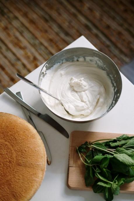 White table with bowl of whipped cream and chopping board with green vegetables