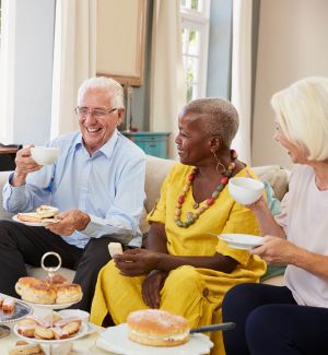 Three older adults, smiling and enjoying an afternoon tea, including cakes and scones, using Lakeland Dairies products