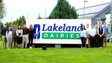 A group of graduates standing in front of the Lakeland Dairies sign