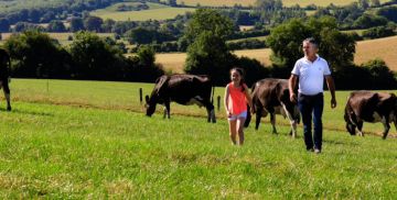 A Lakeland Dairies milk supplier walking with his daughter through fields with rolling hills in the background.