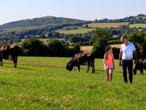 A Lakeland Dairies milk supplier walking with his daughter through fields with rolling hills in the background.