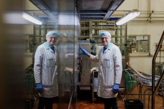 A male operator in PPE is standing in front of a production line of milk, with his reflection opposite him in the machinery.