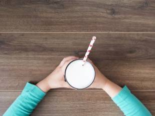 Two arms holding out a glass of milk with a straw
