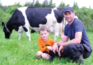 A Lakeland Dairies milk supplier and his young son in a field with a friesian cow.